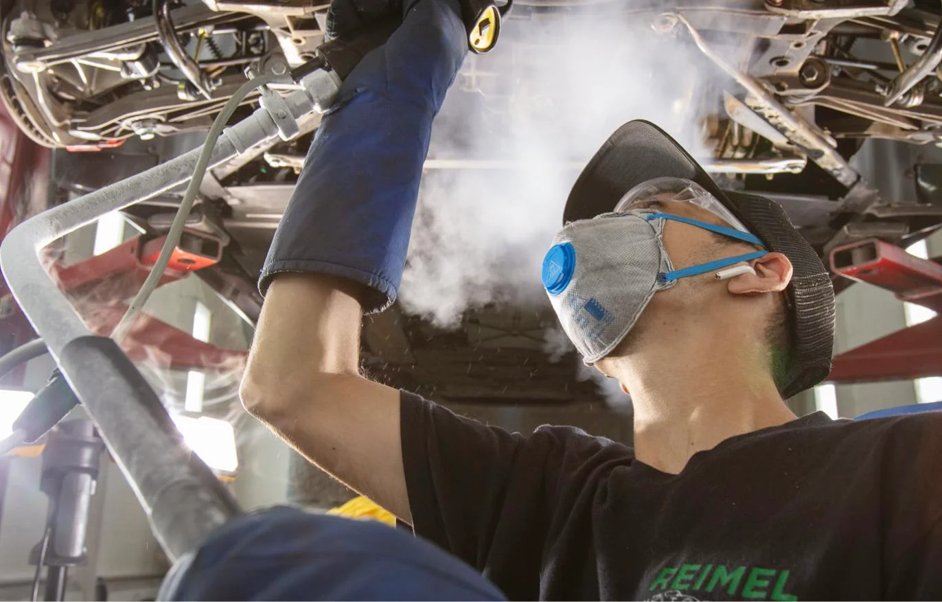 Reimel Motor Cars technician dry ice cleaning a car's undercarriage on the lift